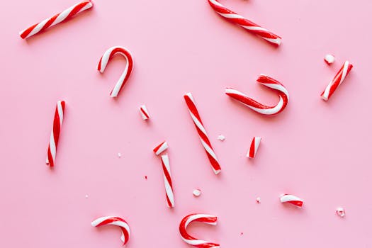 Red and white candy canes scattered on a pink background, symbolizing holiday cheer.