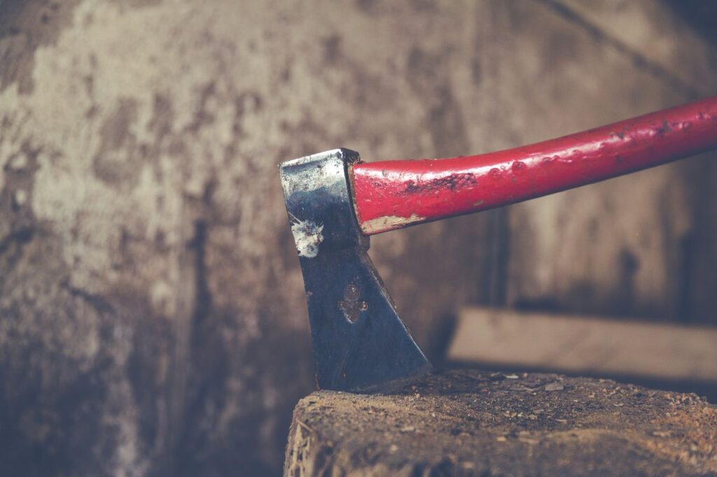 Detailed view of a red handled axe embedded in a wooden stump, outdoors.